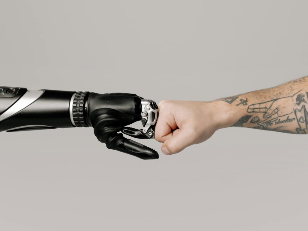 A human fist bumping with a prosthetic arm on a neutral background.