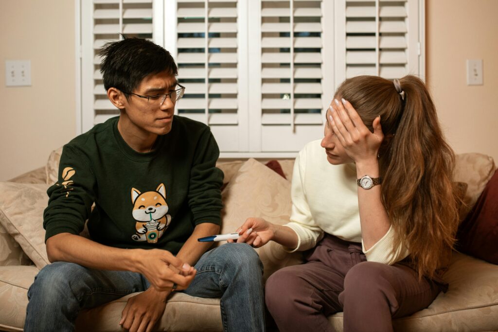 imagen de una pareja con problemas de fertilidad sentada en el sofá de su salón. La chica tiene un dispositivo de test de embarazo en la mano, con expresión de decepción.